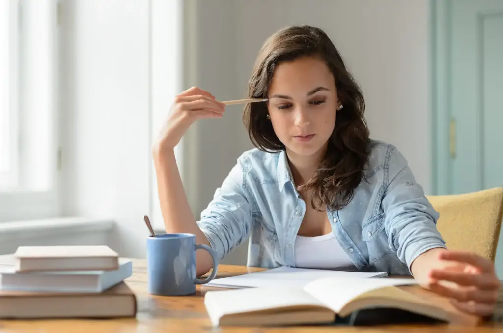 Jovem estudante concentrada, revisando anotações e lendo um livro, preparando-se para o Exame Nacional do Ensino Médio.