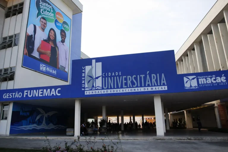 Entrada da Cidade Universitária da FUNEMAC em Macaé, com pórtico azul institucional, prédio acadêmico ao fundo e área de circulação de estudantes no campus.