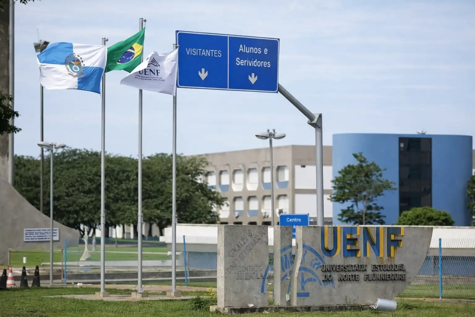 Entrada da UENF em Campos dos Goytacazes, com monumento da universidade, bandeiras e prédios acadêmicos ao fundo, em cena que ajuda a contextualizar a oferta pública de ensino superior na cidade.